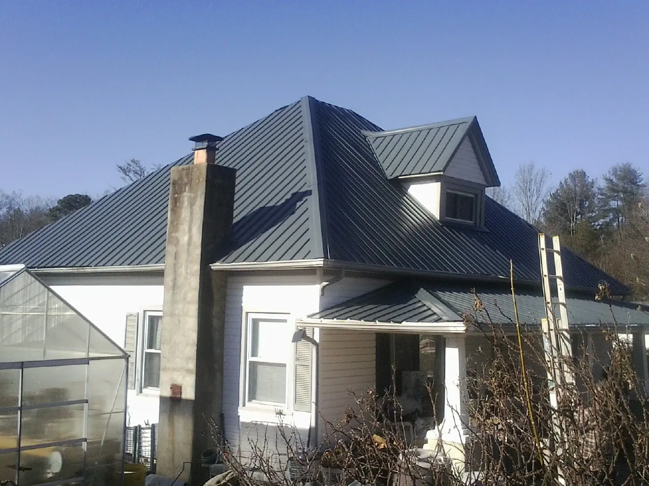 Dark blue standing seam metal roof on a white farmhouse with dormer — Slate & Tile Roof Repair by Roofing Brothers in Clarkfield
