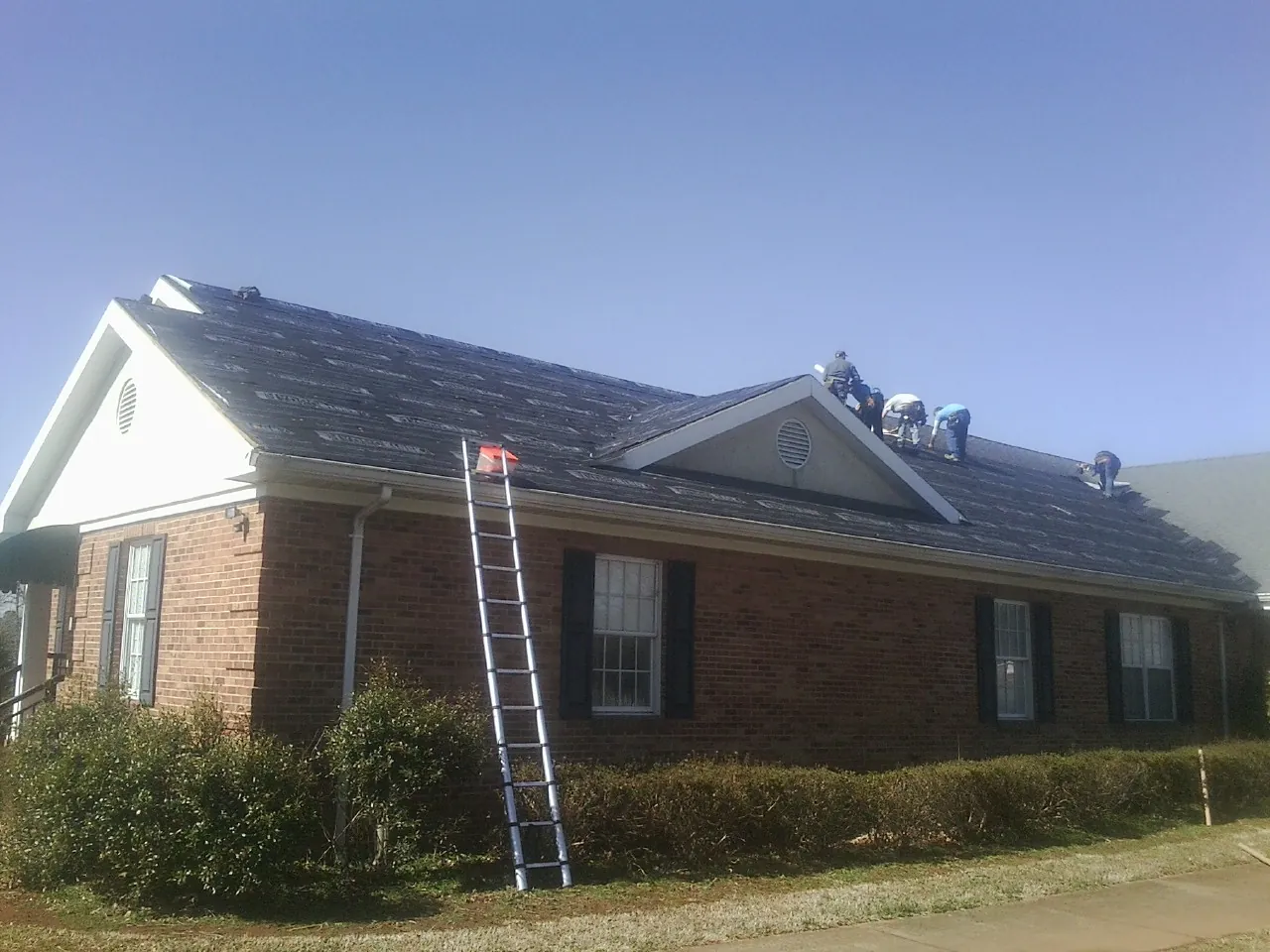 Crew tearing shingles off a brick ranch roof with a ladder set — Metal Roof Repair work by our crew in Clarkfield