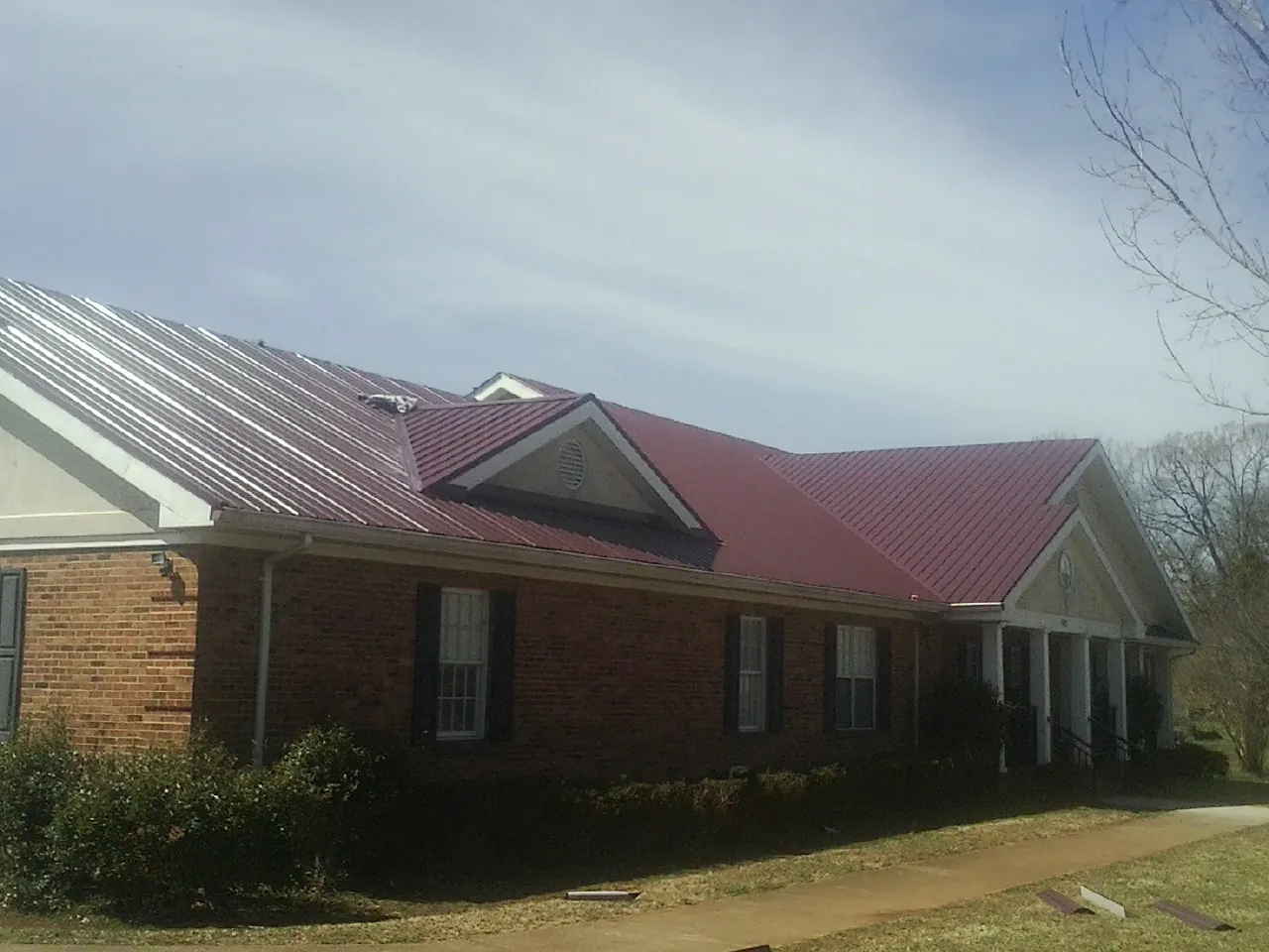 Red metal roof with gabled entries on a long brick building, from a Hail Damage Roof Repair job in Clarkfield