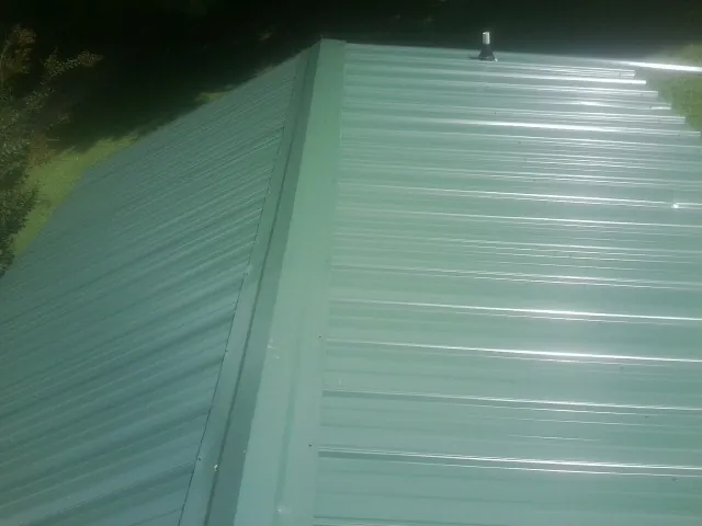 New green metal panels meeting at the ridge of a roof — Flat Roof Repair work by our crew in Clarkfield
