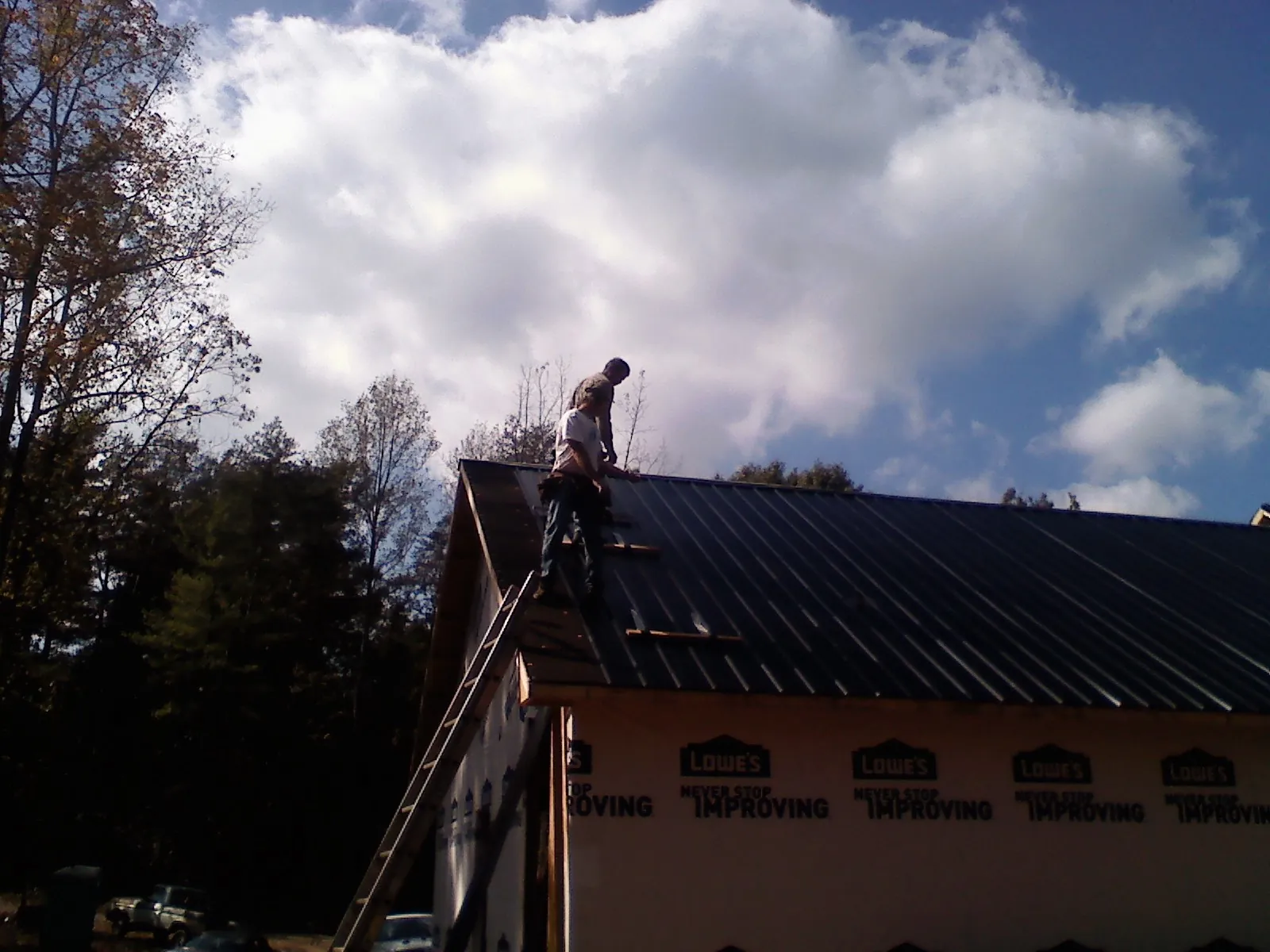 Roofer fastening dark metal panels high against a cloudy sky, from a Roof Inspection job in Clarkfield