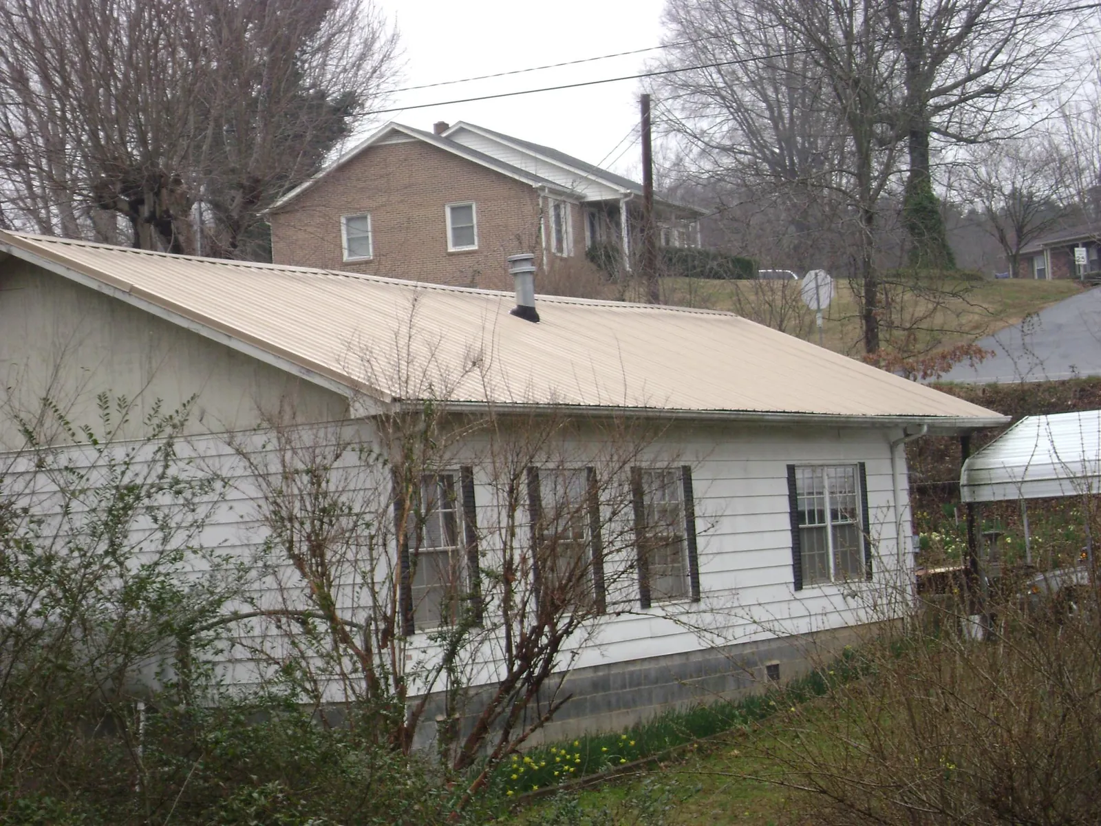 Tan metal roof on a white sided house set into a hillside — Commercial Roofing by Roofing Brothers in Clarkfield